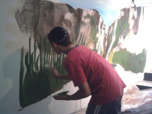 The artist painting reeds at the base of the canyon mural