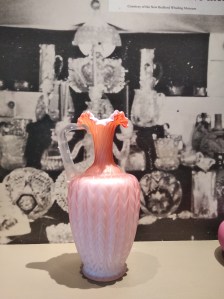 Ruffled pink glass vase in front of an archival exhibition photograph