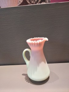 Pink and white satin glass pitcher in a museum display case