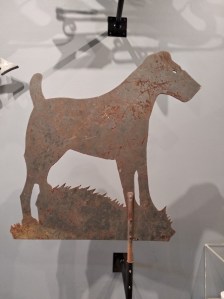 Rusted iron terrier weathervane mounted in a museum case