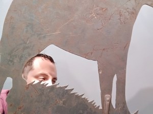 Nachliel Selavan looking through the cut-out of a rusted elephant weathervane