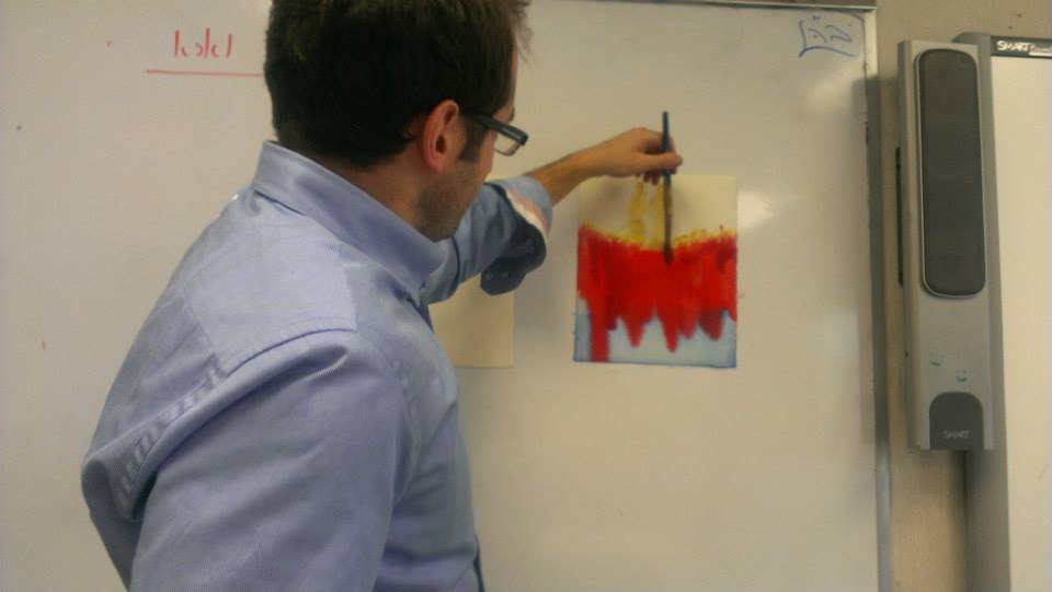 Nachliel Selavan drawing at an easel in the classroom, working red pastel and water into the Nile